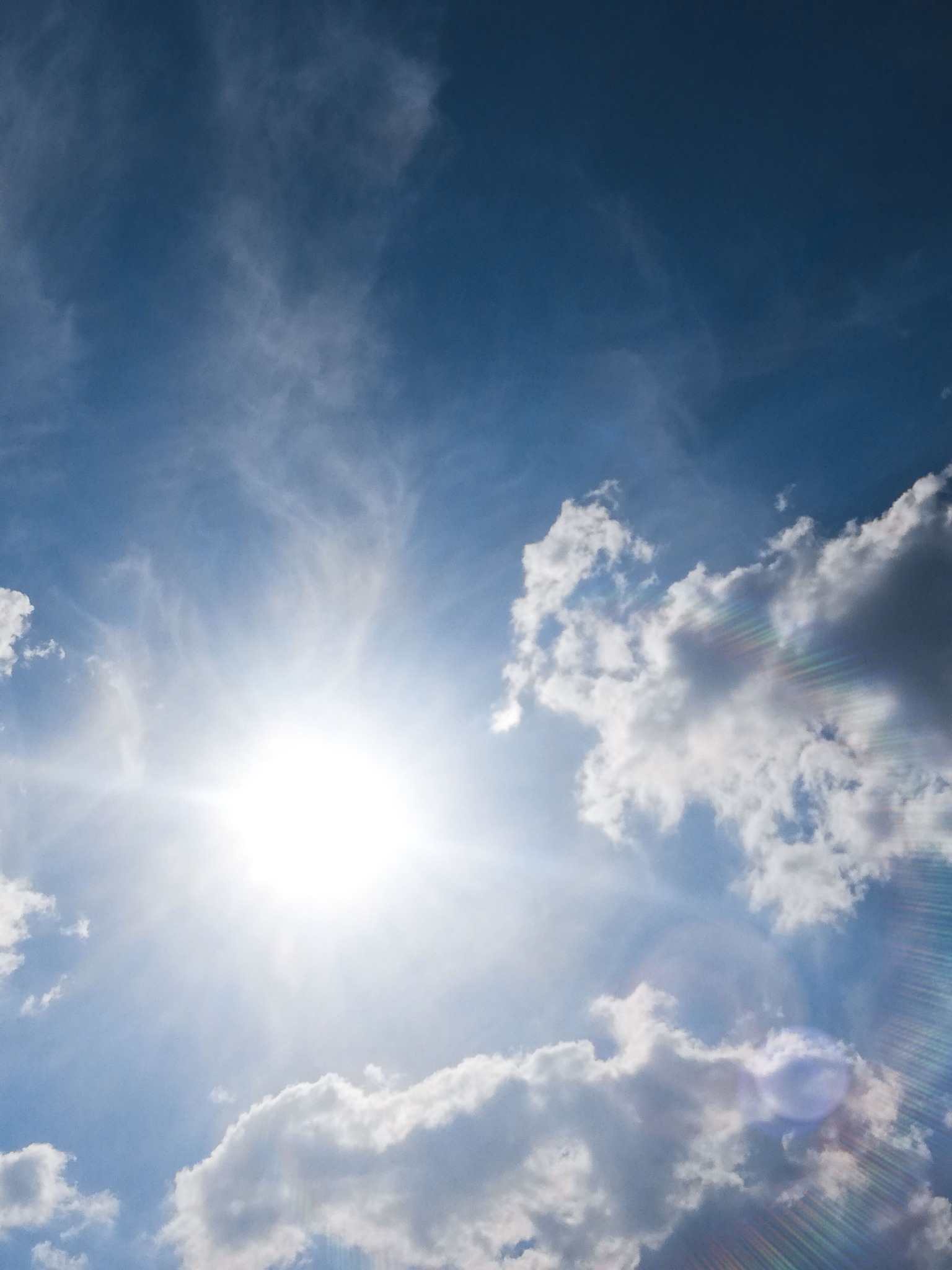 Strahlende Sonne zwischen weißen Wolken vor blauem Himmel